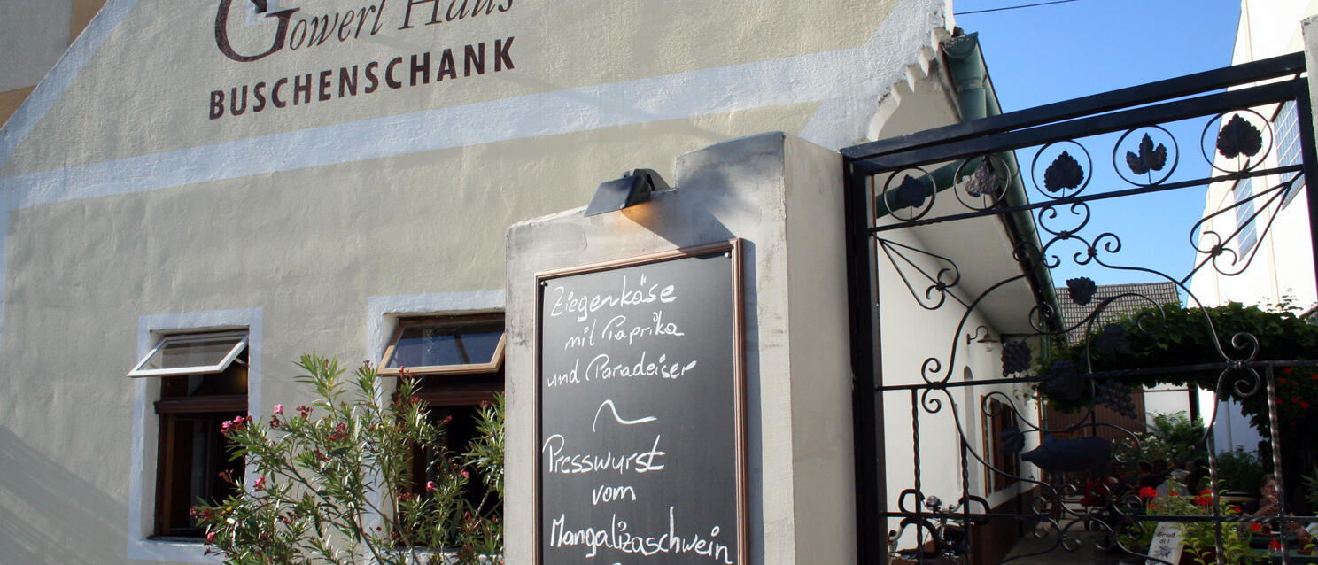 Außenansicht der Buschenschank „Gowerl Haus" mit Kreidetafel und schmiedeeisernem Tor.