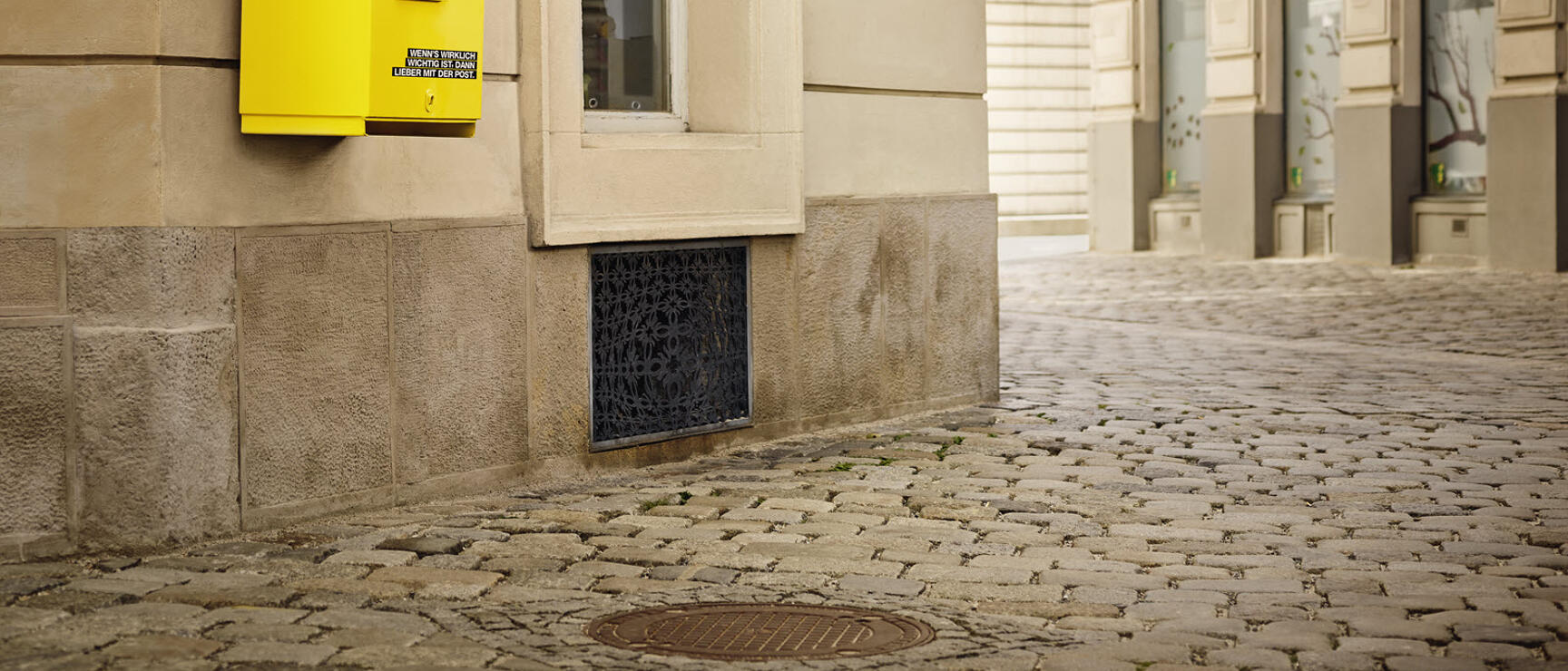 Yellow mailbox on house facade, sign reading "Gasthof zur Post", cobblestone street, Vienna.