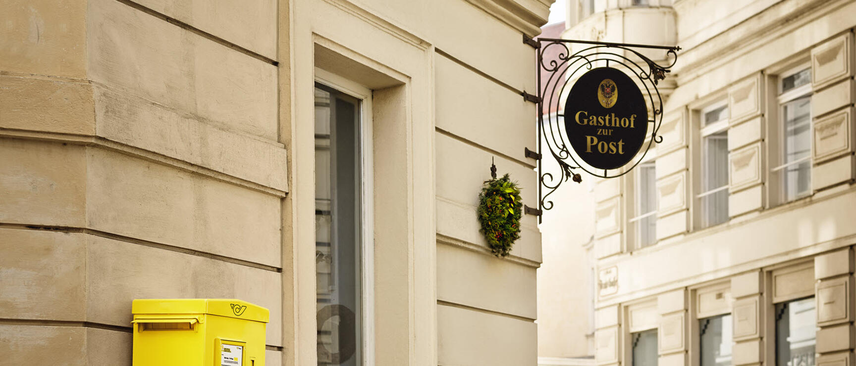 Gelber Briefkasten an Hausfassade, Schild „Gasthof zur Post", Kopfsteinpflasse, Wien.