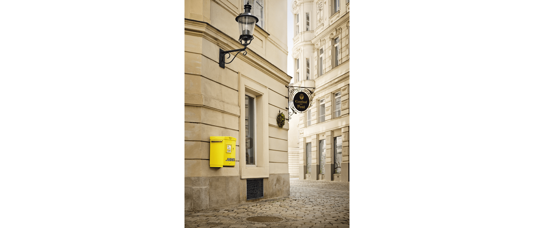 Yellow mailbox on house facade, sign reading "Gasthof zur Post", cobblestone street, Vienna.