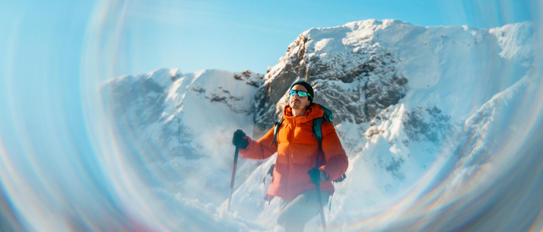 A snowshoer stands in the middle of a snow-covered mountain landscape, gazing out into the winter expanse. The circular reflections of light lend the scene a special atmosphere and emphasize the sense of tranquility, freedom, and connection to nature in the Austrian Alps.