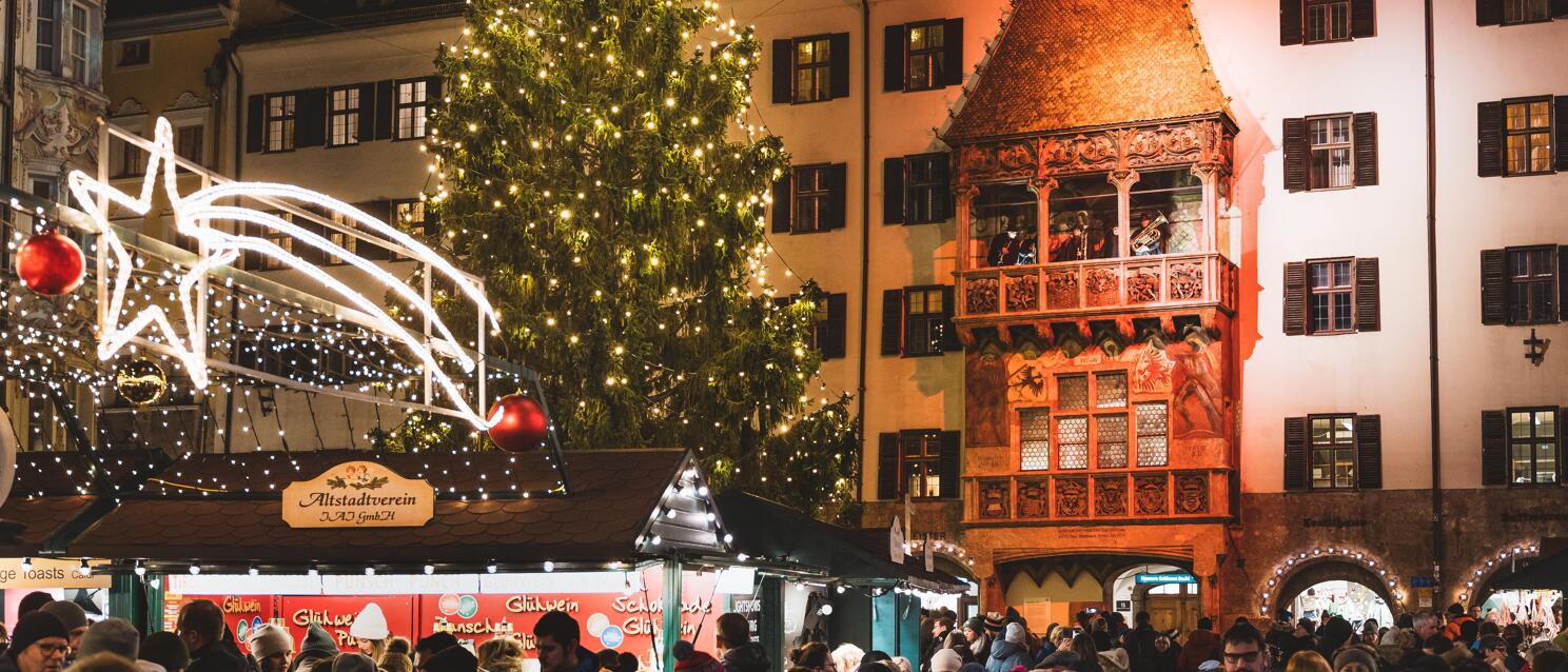 Christkindlmarkt in front of the Golden Roof in Innsbruck at night, illuminated Christmas tree, crowds of people.