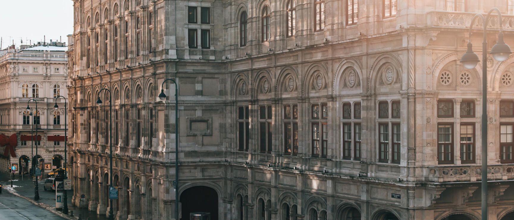 Vienna State Opera backlit by winter sun with snowy street in front, Vienna.