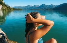 Woman in bikini with wet hair at the lake shore, turquoise water and mountain panorama in the background.
