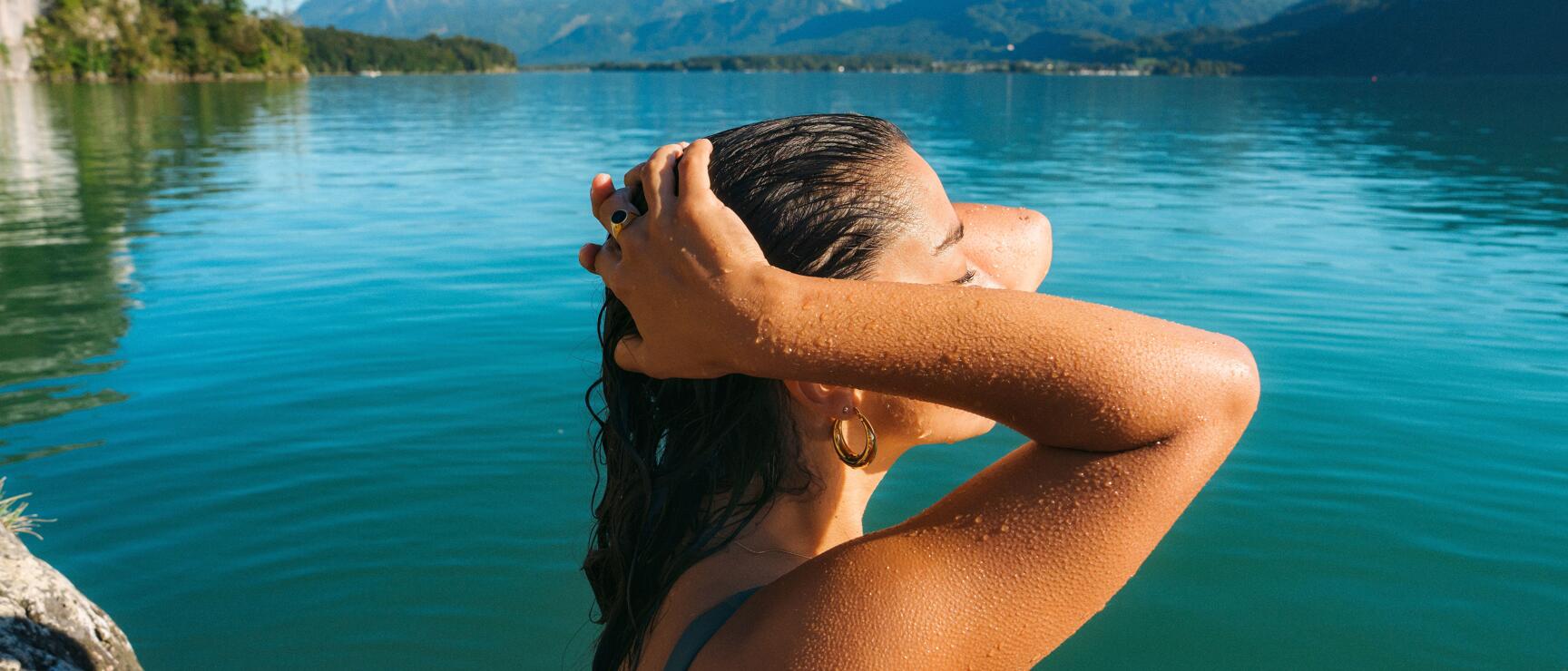 Woman in bikini with wet hair at the lake shore, turquoise water and mountain panorama in the background.