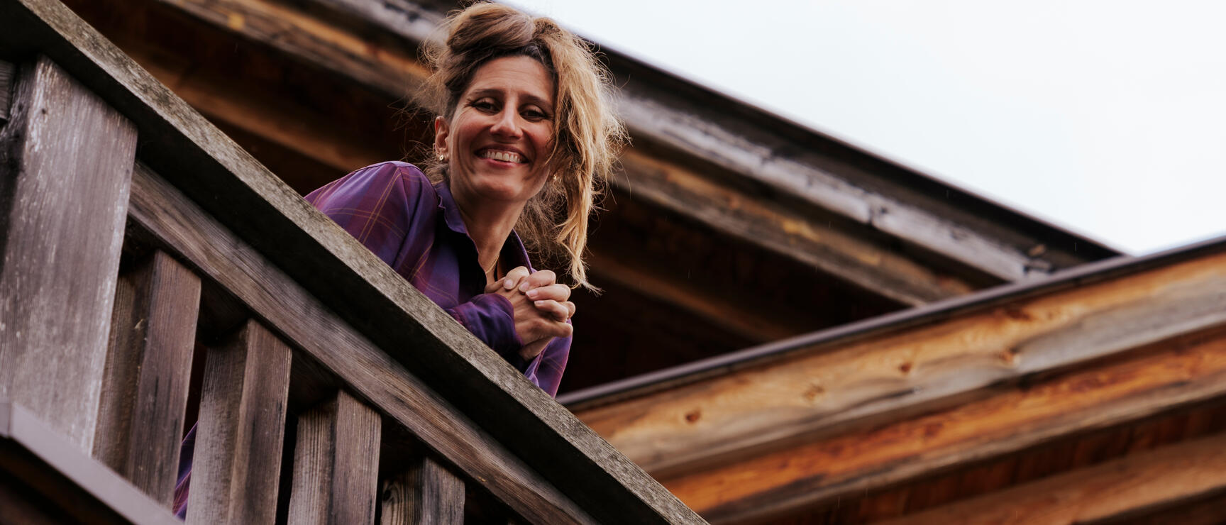 Smiling woman leaning over wooden railing of an old wooden building, worm's eye view.