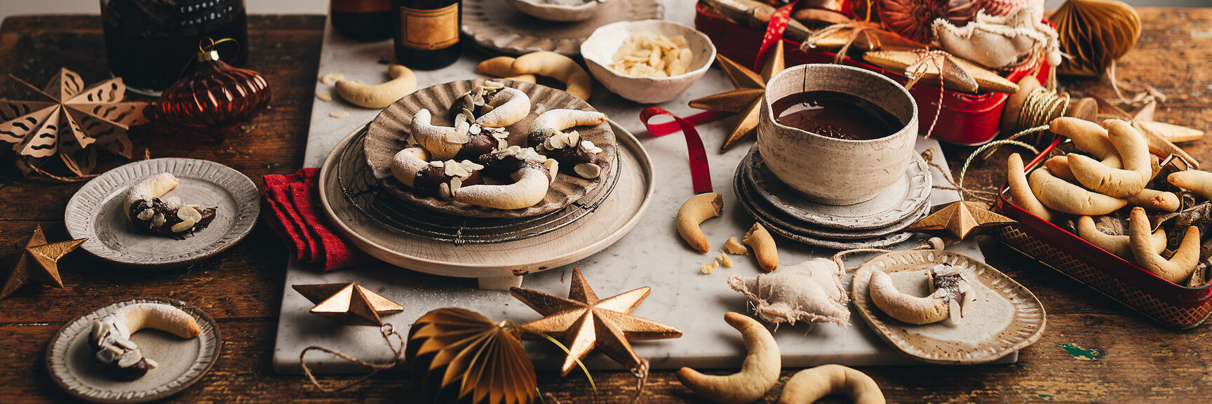 Vanilla crescents with chocolate on plate, cup of hot chocolate, Christmas decorations and spice bottles on wooden table.