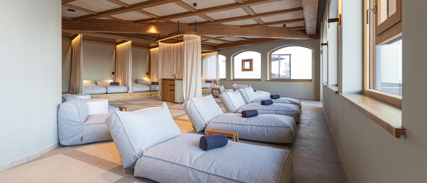 Spa relaxation room with grey loungers, folded towels and wooden ceiling with coffered structure.