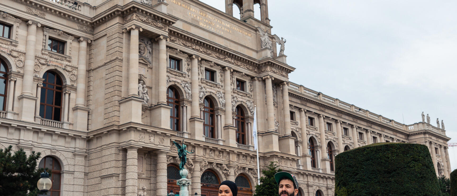 Two people strolling in front of the Museum of Art History Vienna with manicured lawns in the foreground.