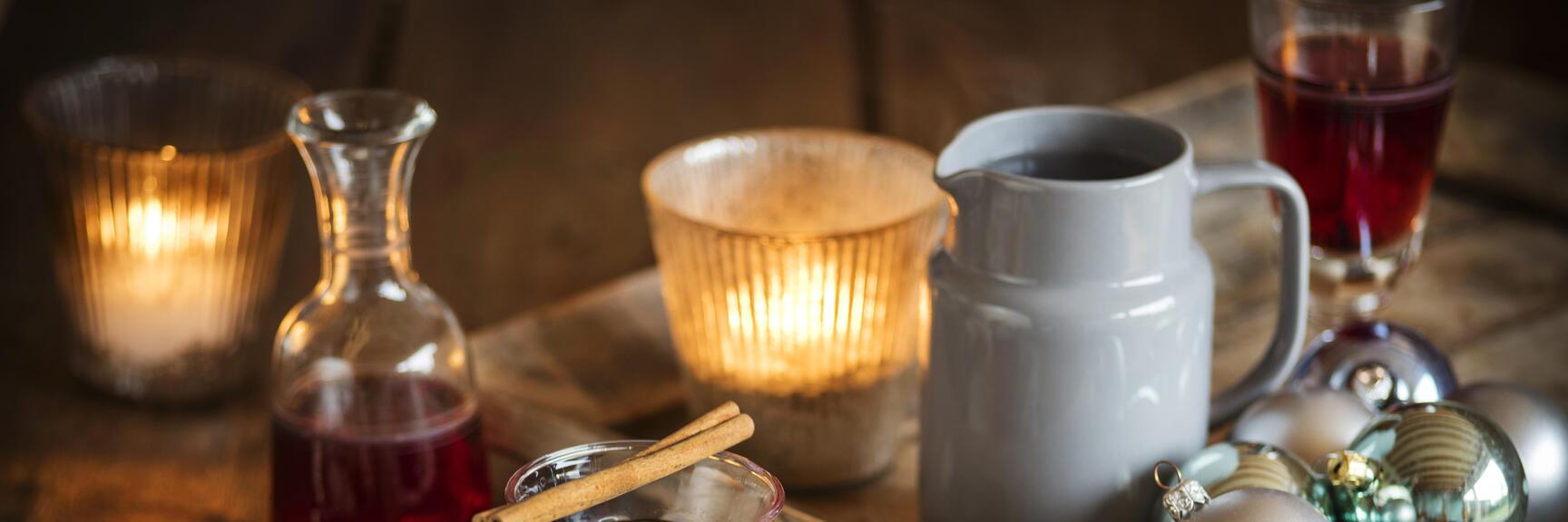 Mulled wine with cinnamon stick in a glass, Christmas cookies and baubles on a wooden table with candles.