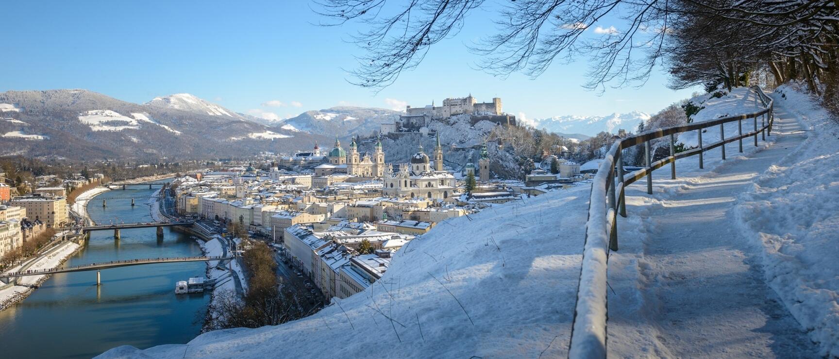 Winter view of Salzburg's old town with Hohensalzburg Fortress, Salzach River and snow-capped mountains.