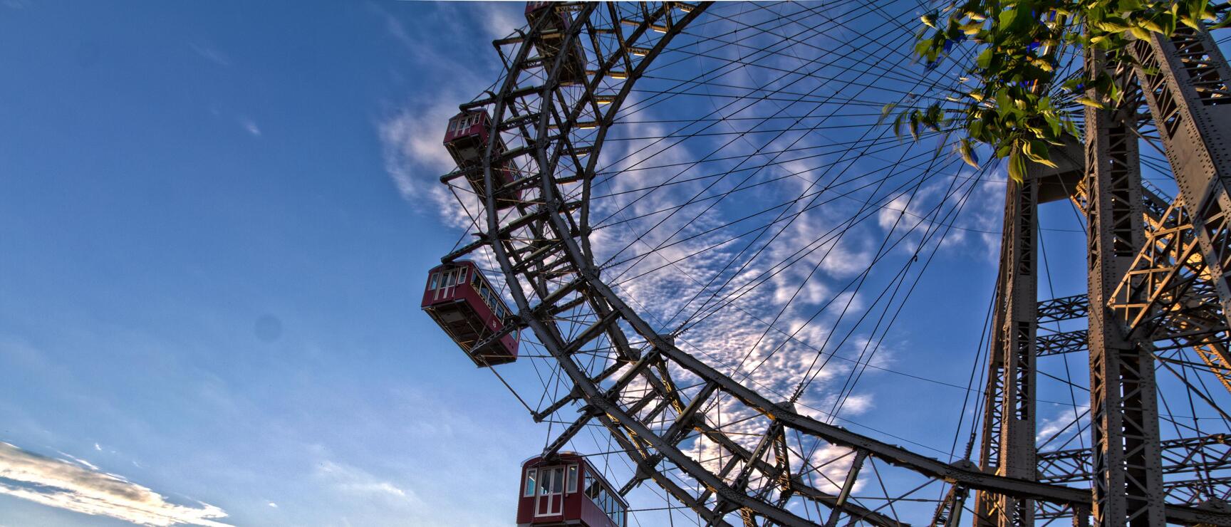 Vienna Giant Wheel in Prater at sunset, red gondolas against blue sky.