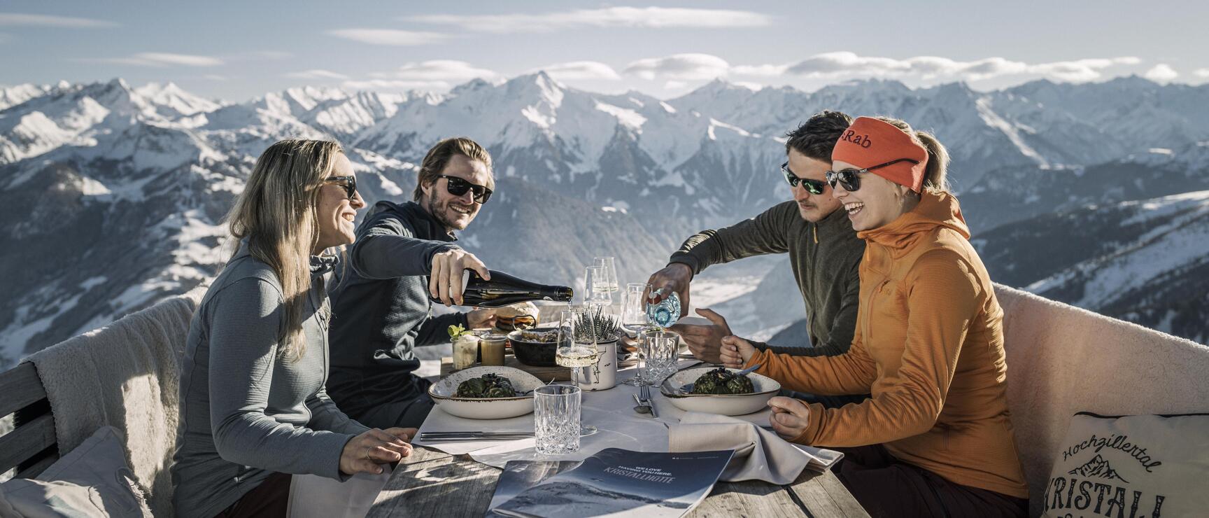 Four people dining on mountain hut terrace with snow-capped Alps in background, Zillertal.