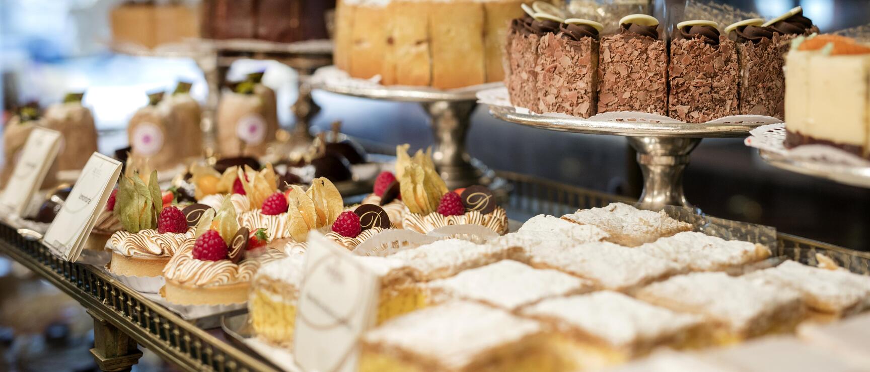 Pastry shop display with chocolate cake, tarts with raspberries, physalis and powdered sugar pastries