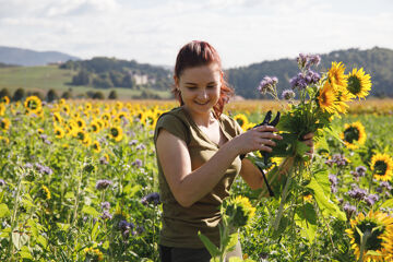 Eine Frau steht mit einem Blumenstrauß in einem Feld, Urlaub am Bauernhof