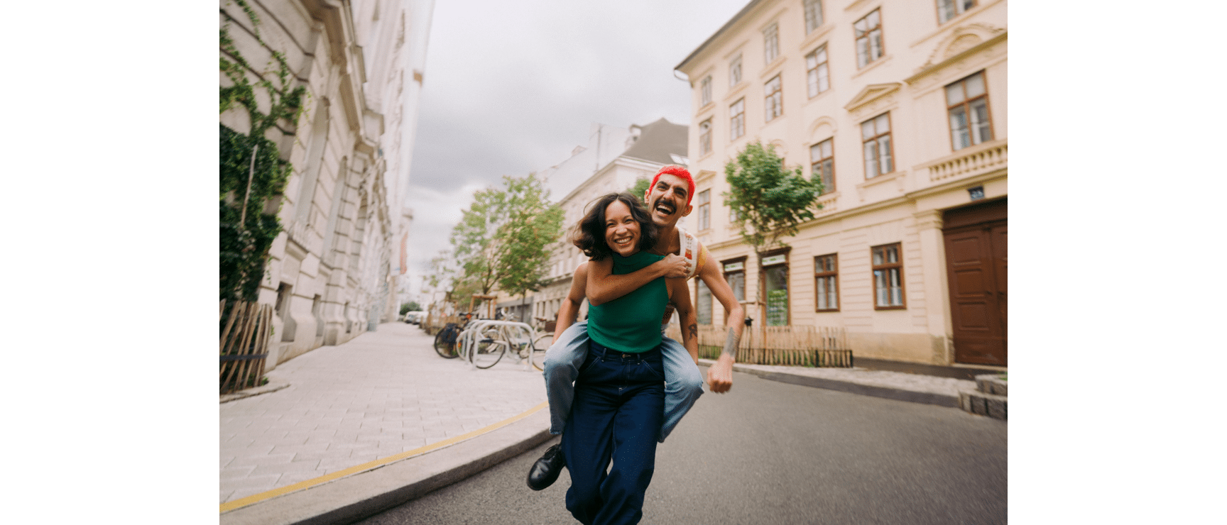Red-haired man carrying laughing woman piggyback on a Vienna city street.