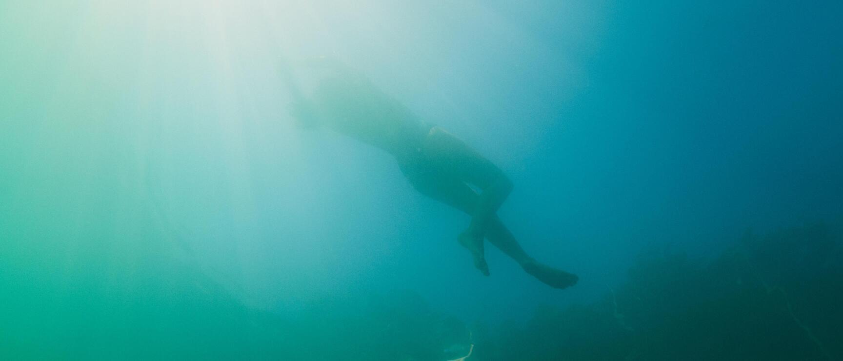 Taucher mit Flossen unter Wasser, türkis-blaues Licht von oben, Unterwasseraufnahme.