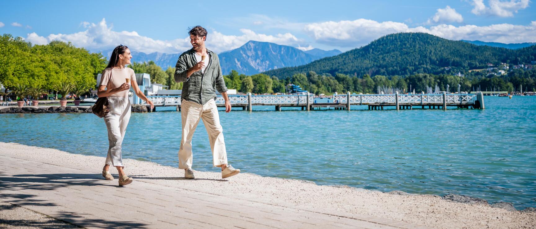 Couple walking along the eastern bay of Lake Wörthersee with a view of the Karawanken mountains