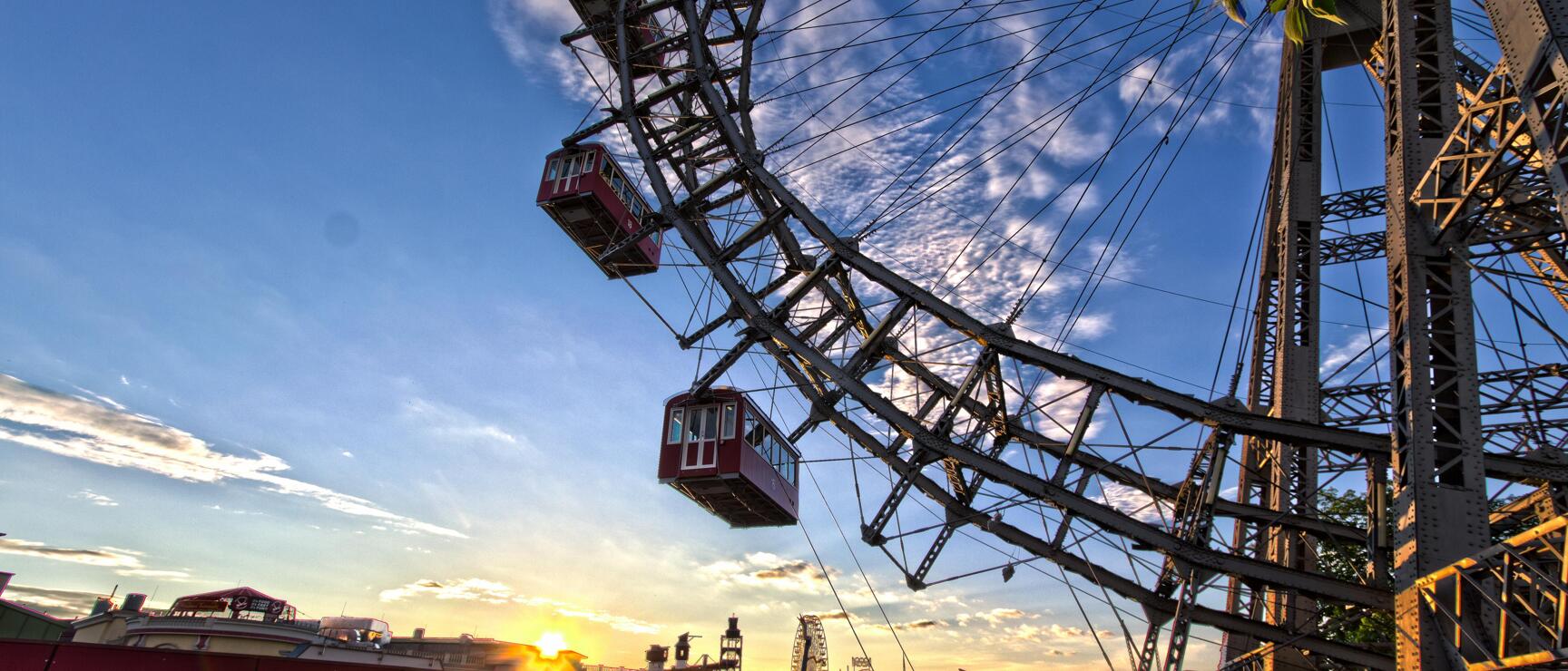 Vienna Giant Wheel in Prater at sunset, red gondolas against blue sky.