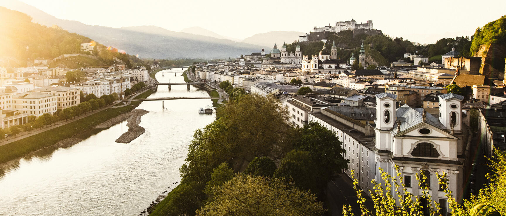 Panoramic view of Salzburg with Salzach river, old town, cathedral and Hohensalzburg Fortress in warm evening light.
