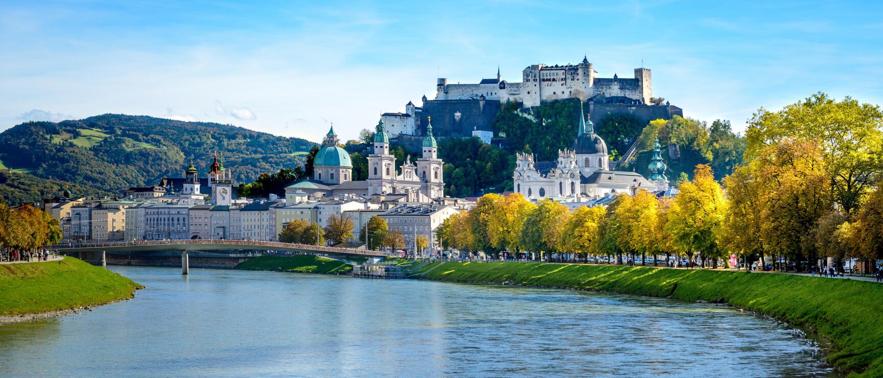 Salzburg old town with cathedral, churches and Hohensalzburg Fortress above the Salzach River, autumn trees.