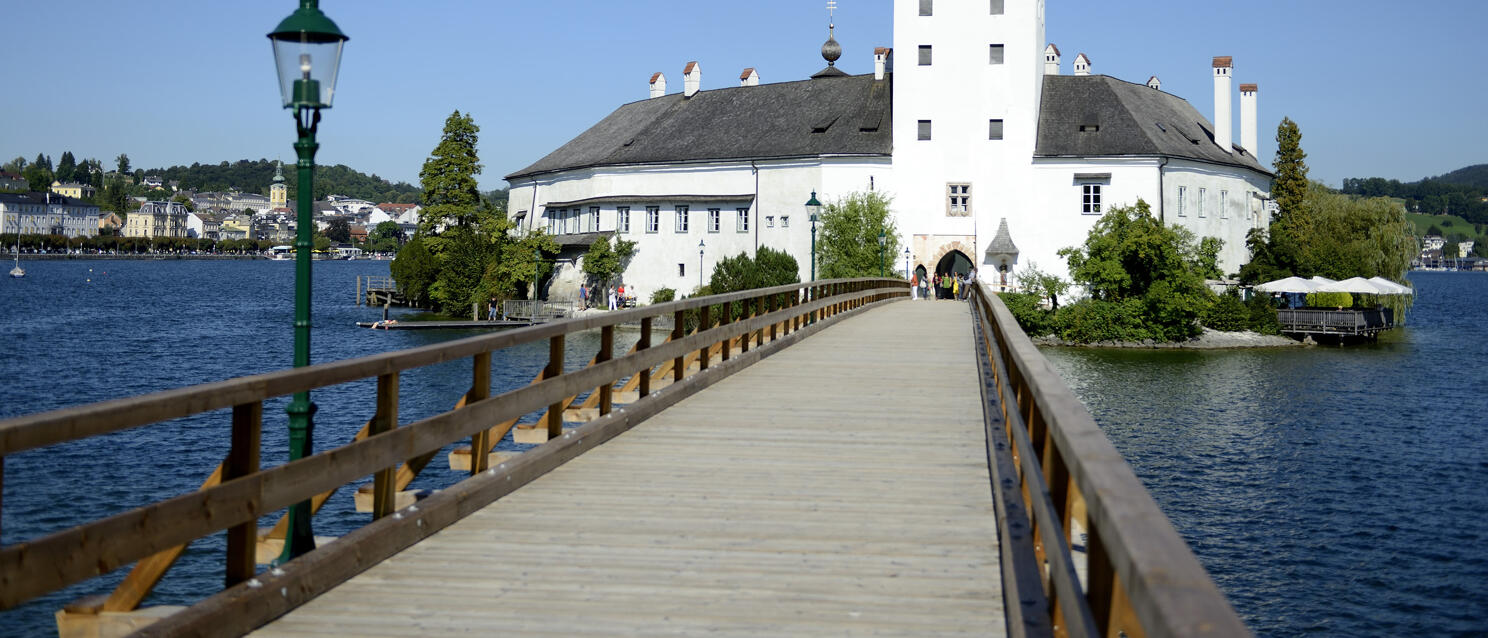 Wooden boardwalk leading to Ort Castle on an island in Lake Traun, Gmunden in the background.