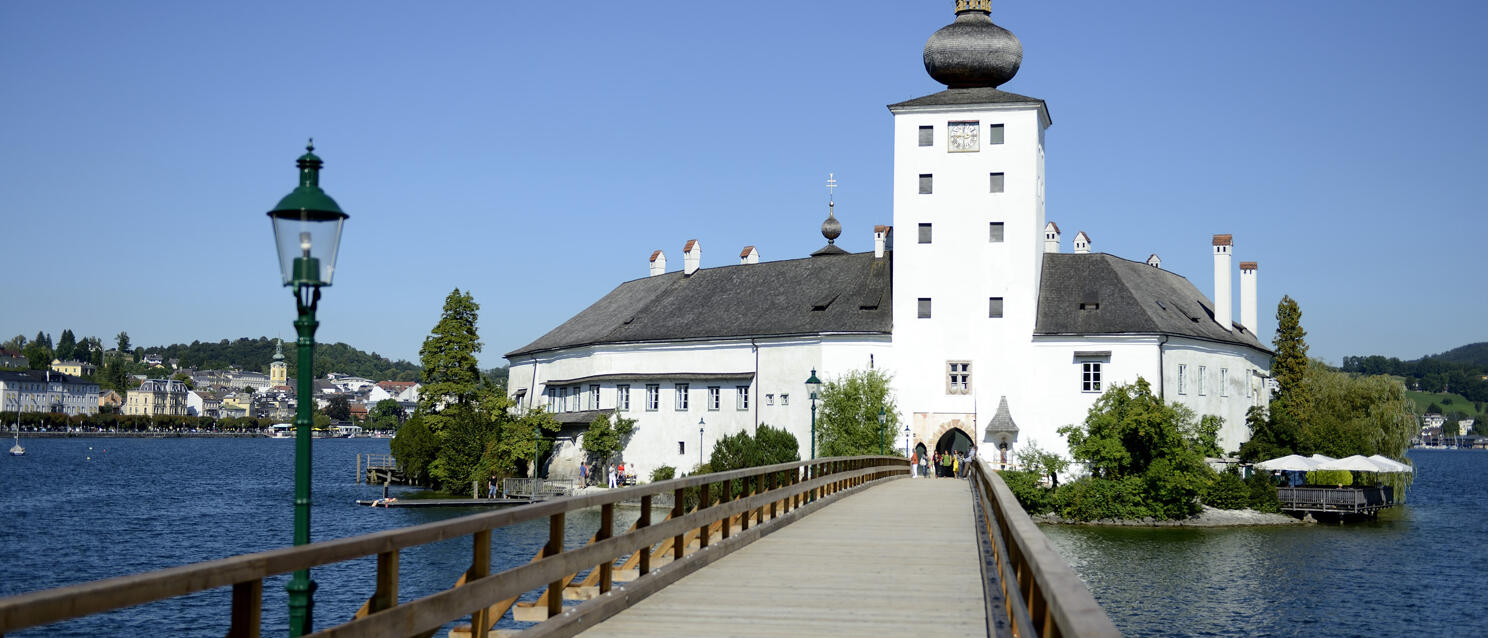 Wooden boardwalk leading to Ort Castle on an island in Lake Traun, Gmunden in the background.